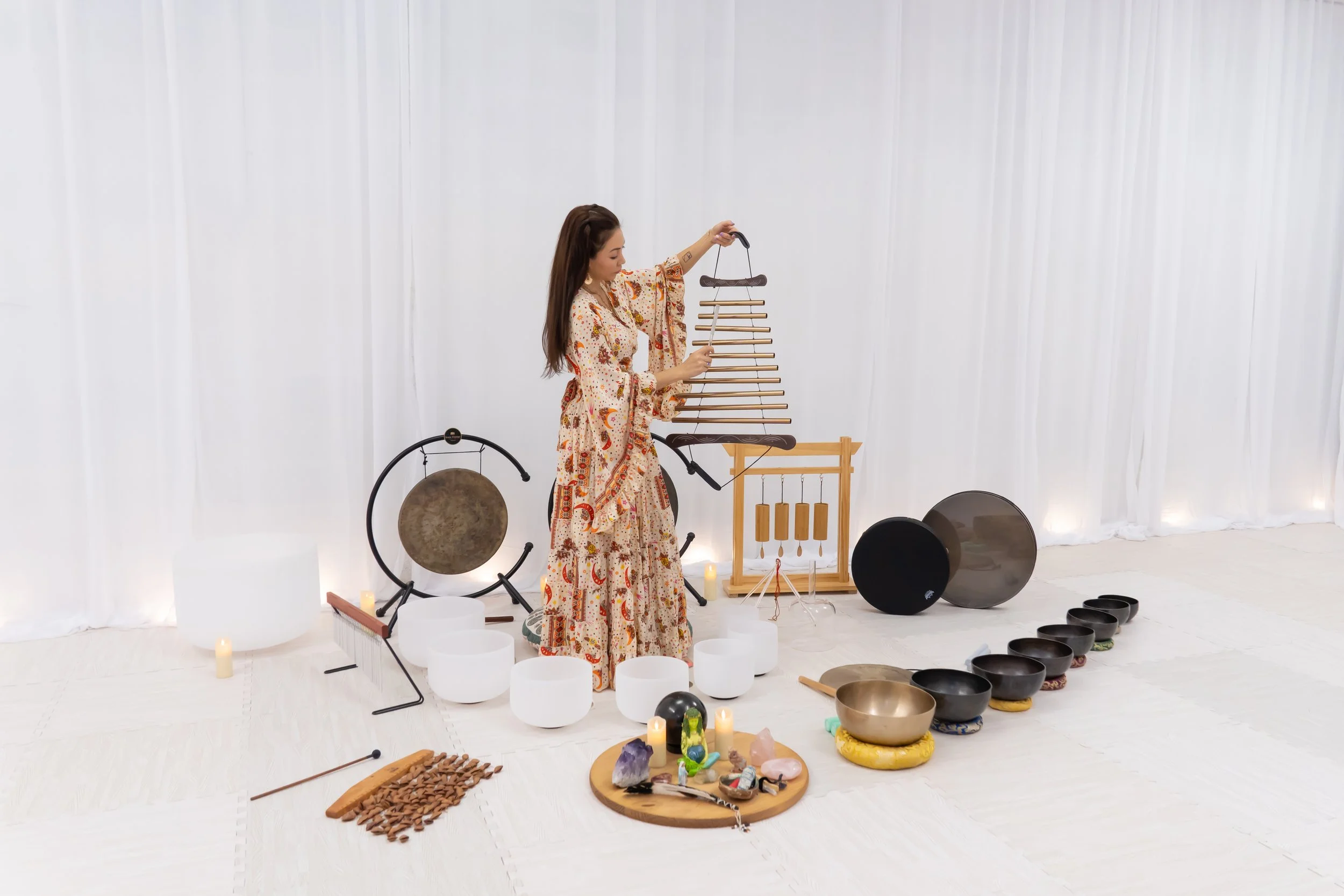 woman holds sound healing instrument surrounded by drums, bowls, gong, white curtains and white floor by photographer Lenee Love