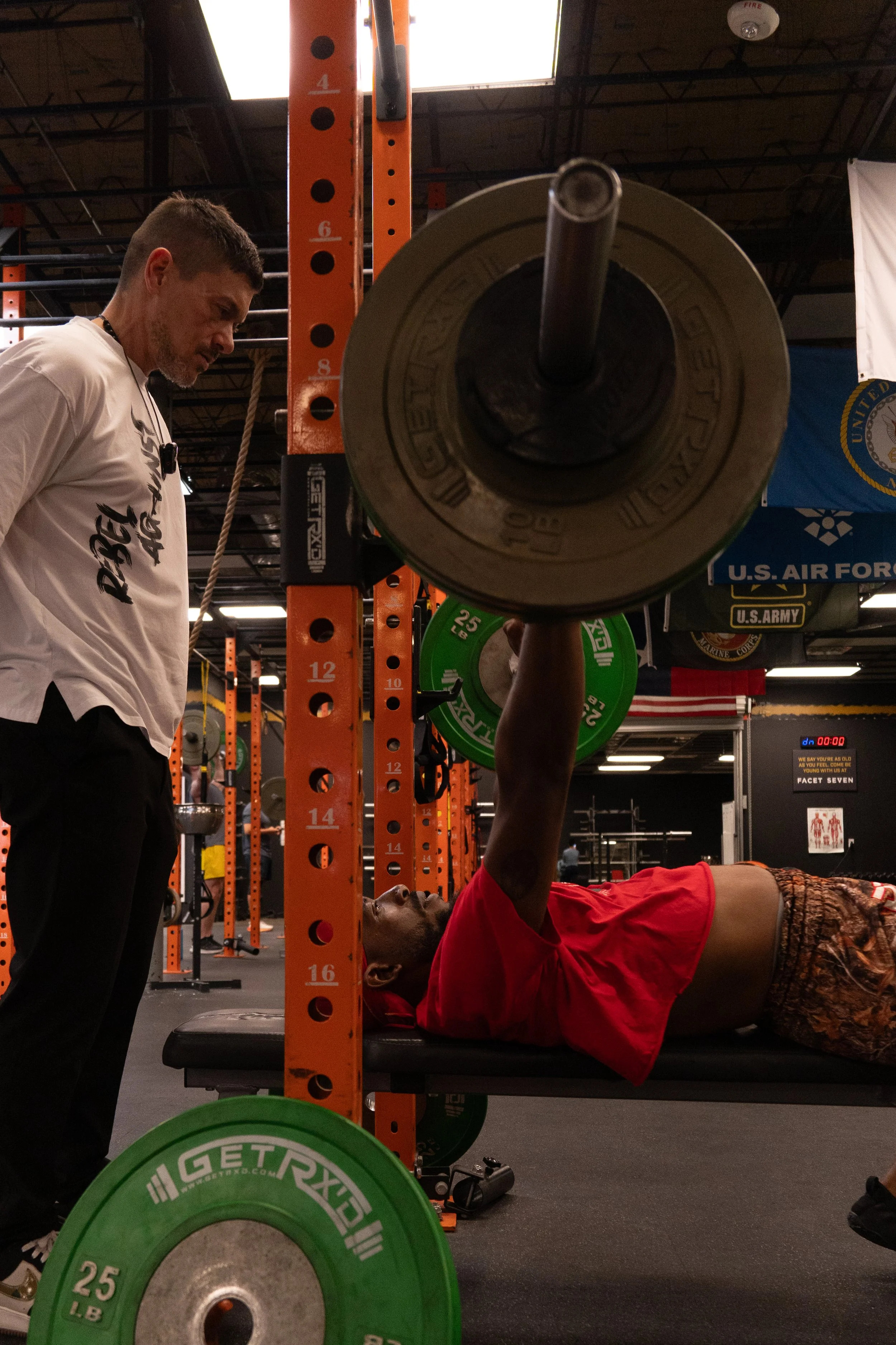 man in crop top bench pressing with trainer watching over him at facet seven gym in houston by photographer Lenee Love