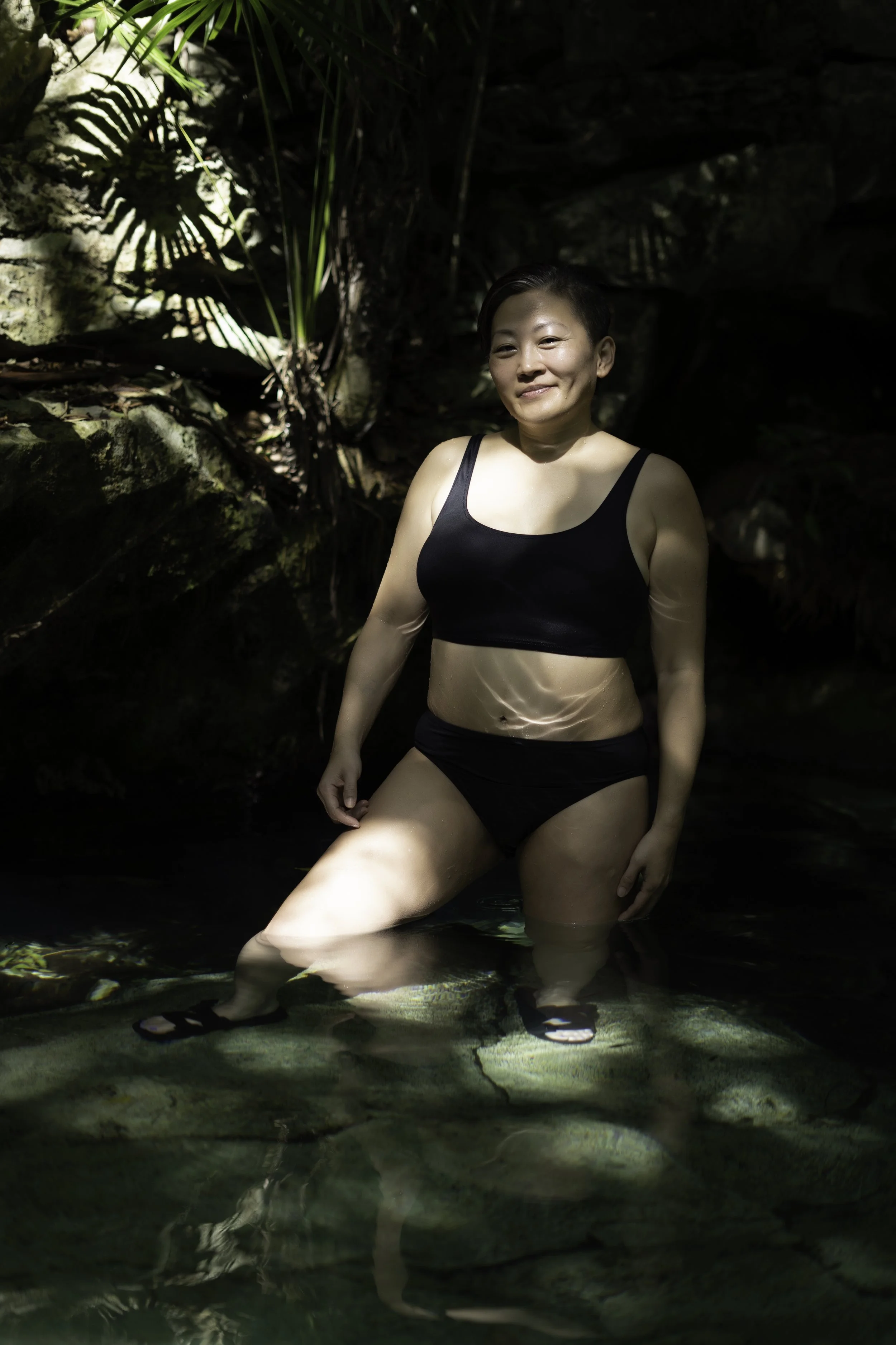 Asian woman in black two piece bathing suit poses in a cenote light and shadow by photographer Lenee Love