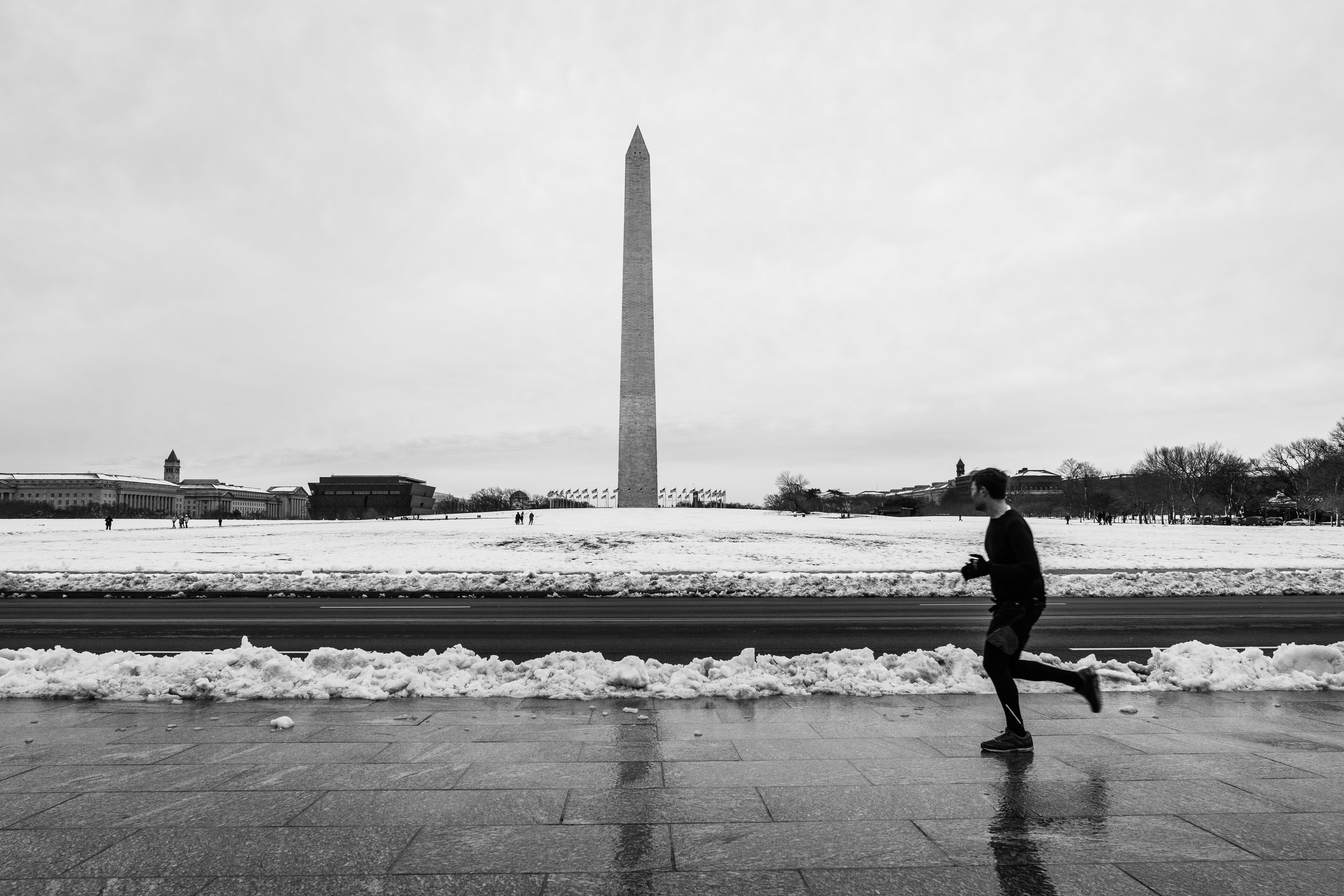 A black and white image of a runner in front of the George Washington monument during a snow day. 
