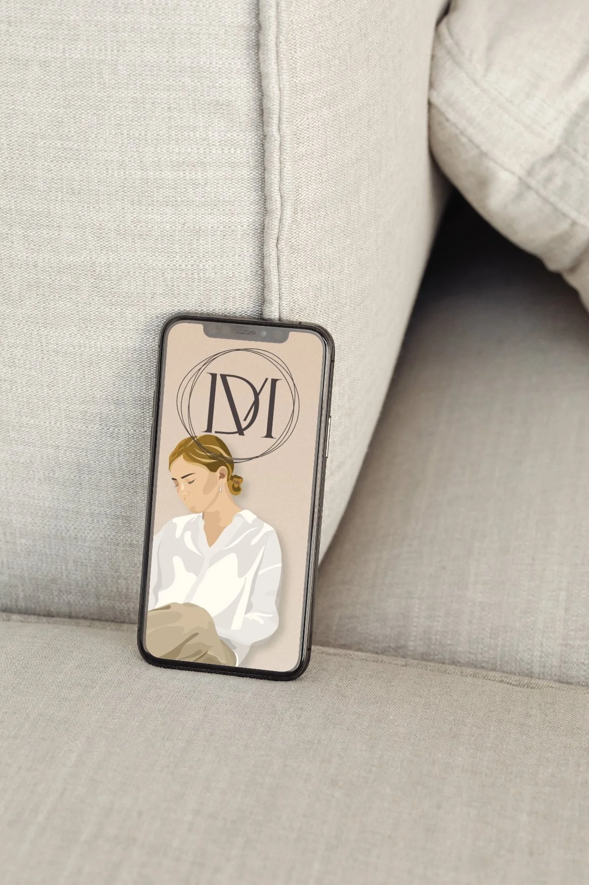Smartphone leaning on a beige couch, displaying an artistic illustration of a woman in a white blouse with a logo at the top.