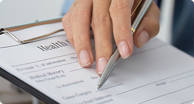Close-up of a person signing a health form with a silver pen.