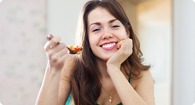 A young woman smiling and eating a spoonful of food at home.
