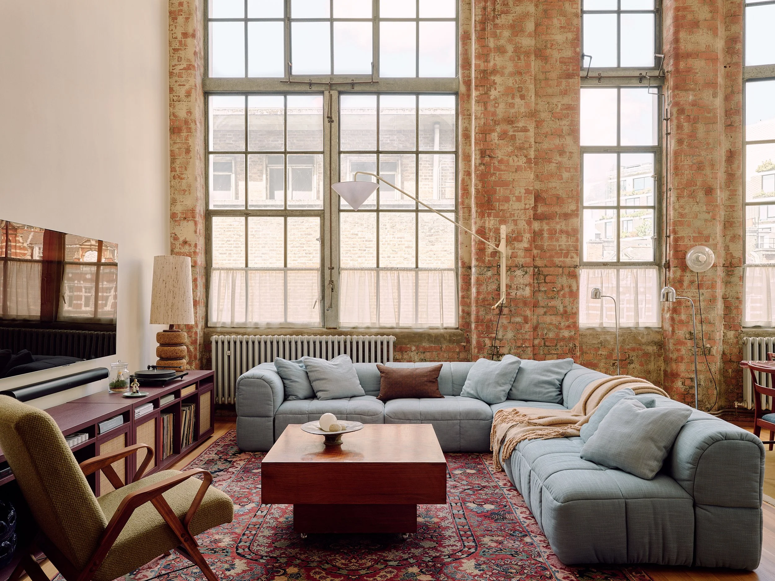 Retro living room with antique Persian rug and cornflower blue Arflex Strips sofa in Farringdon loft, London interior design by Duelle Studio