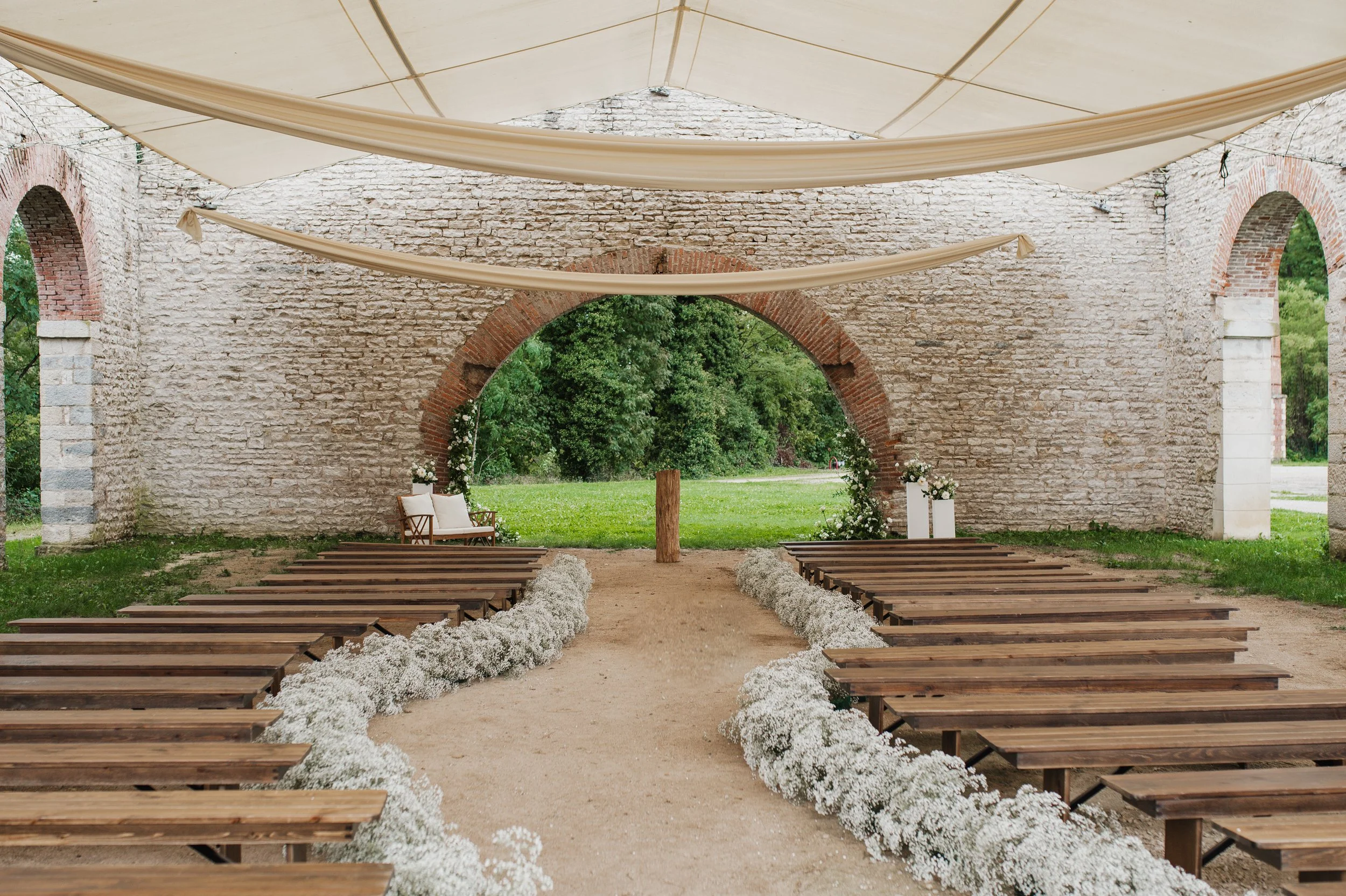 décoration de cérémonie de mariage en plein air sous des arches en pierre, avec des bancs en bois et des décorations florales