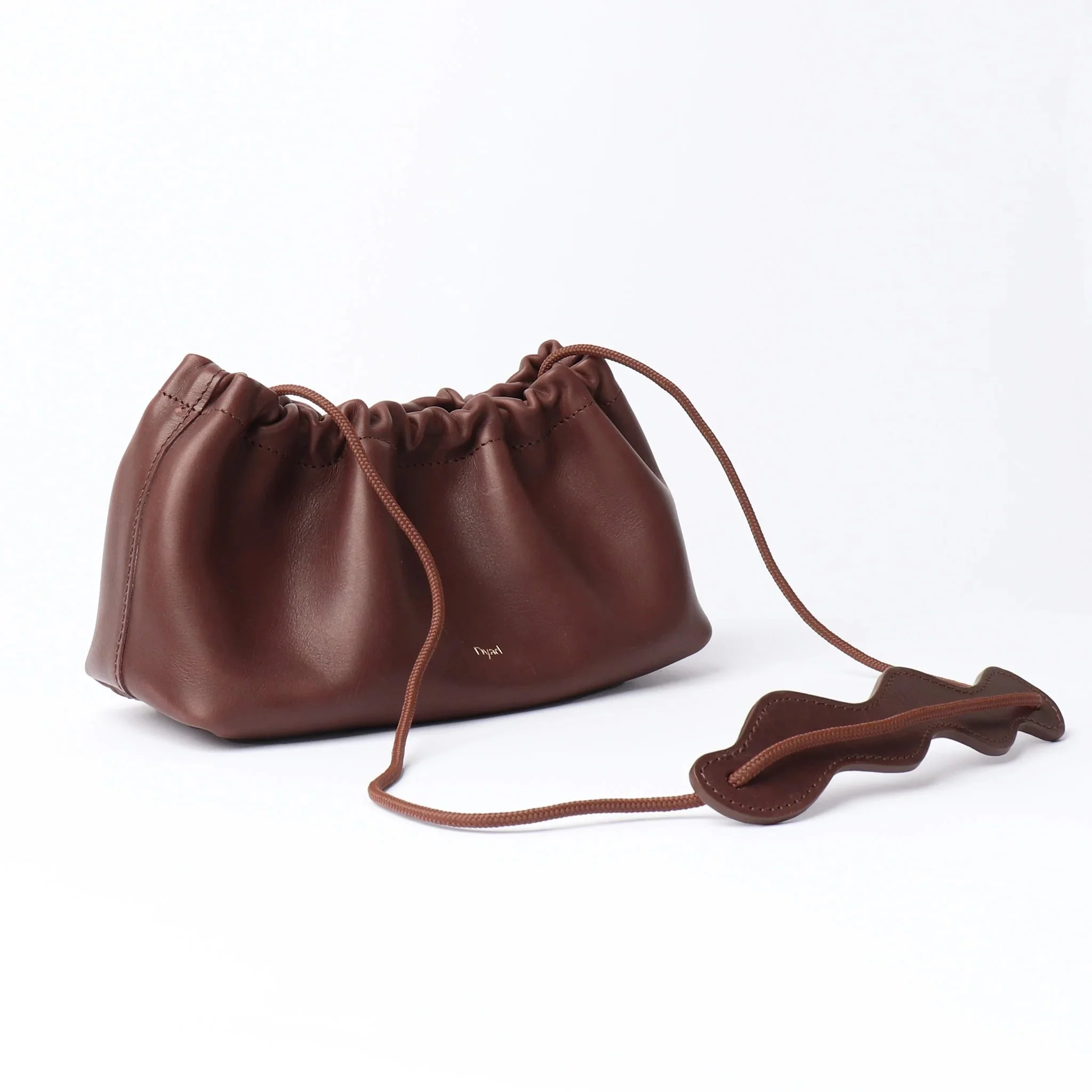 Chocolate brown pleated canvas shoulder bag by Project Dyad with adjustable strap and minimalist silhouette.