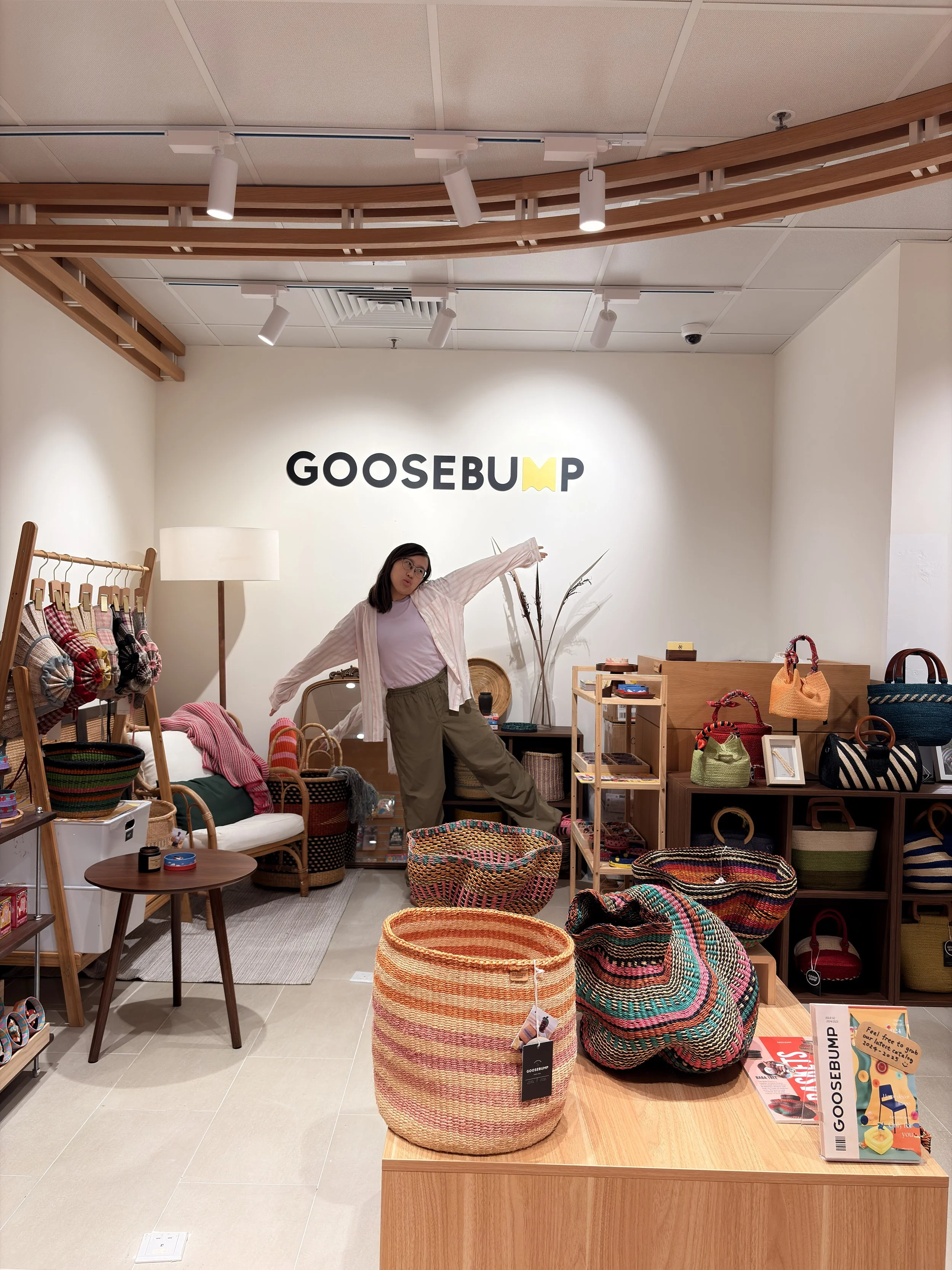A woman in a boutique store with woven baskets and handbags on display, and the store sign "GOOSEBUM" on the wall behind her.