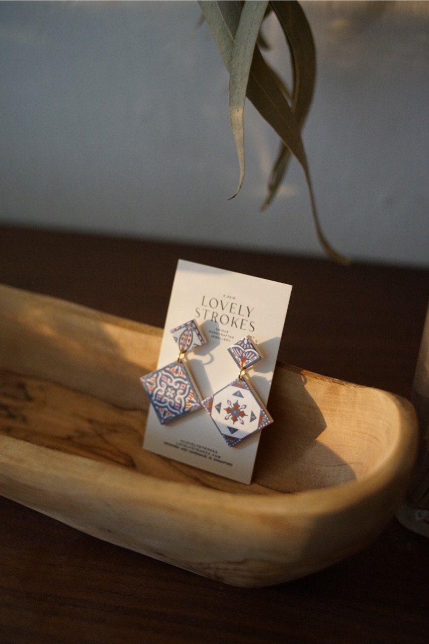 A pair of handcrafted tile-inspired earrings with intricate hand-painted patterns in warm tones, evoking Mediterranean and Moroccan artistry, perfect for fashion and cultural art enthusiasts.