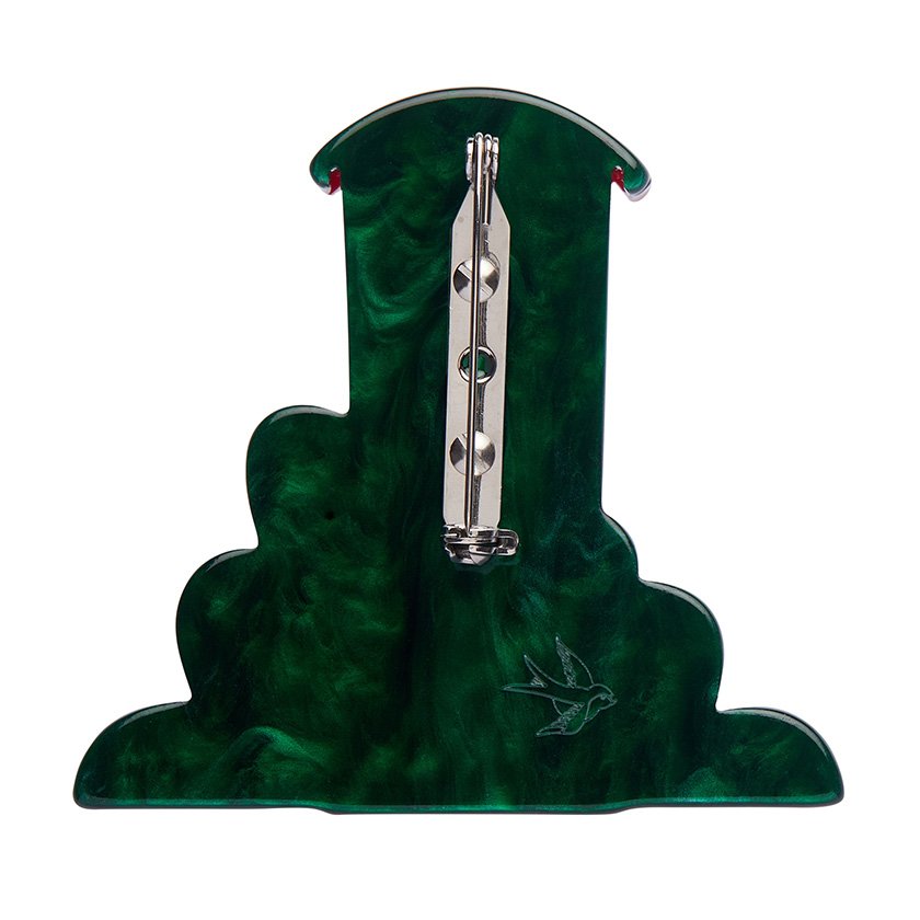 A brooch shaped like a vibrant red telephone booth, surrounded by green foliage with floral details, hand-assembled using resin, representing London’s iconic charm.