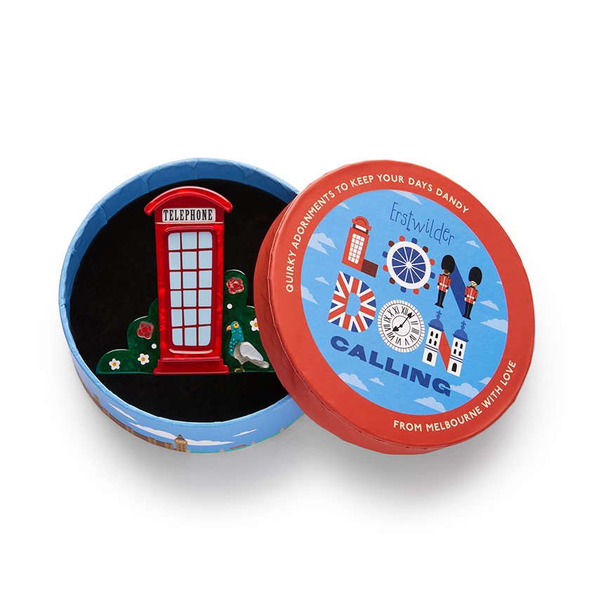 A brooch shaped like a vibrant red telephone booth, surrounded by green foliage with floral details, hand-assembled using resin, representing London’s iconic charm.