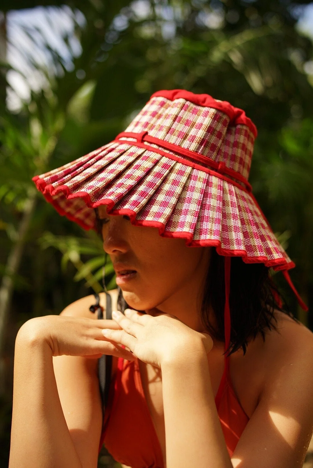 一名女性戴著格子紋太陽帽，帽緣有紅色飾邊，身處熱帶環境。