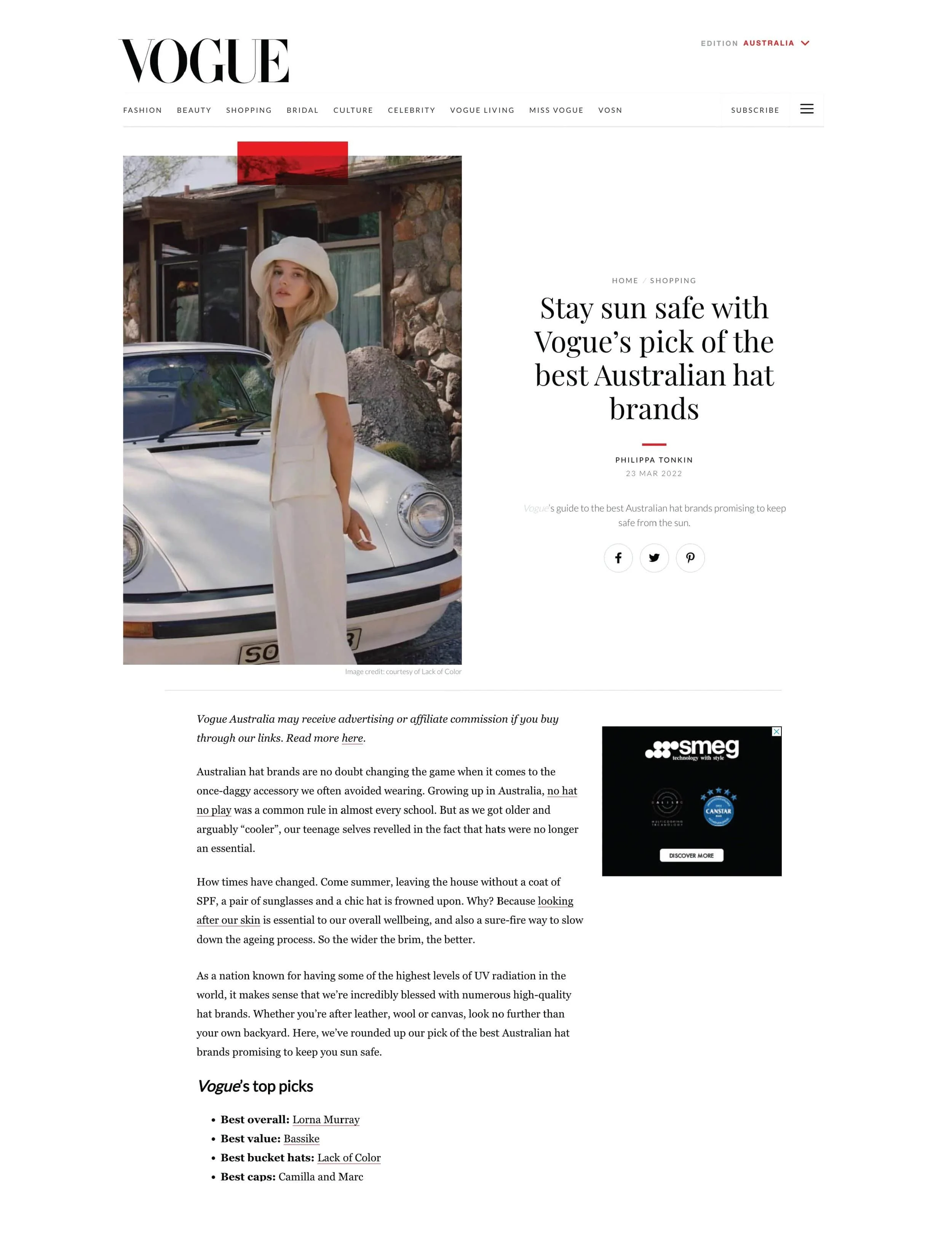 一名女性穿著白色衣服，戴著寬簷帽，站在白色經典車旁，戶外，面對著一棟樸素的石頭建築，在陽光明媚的日子。