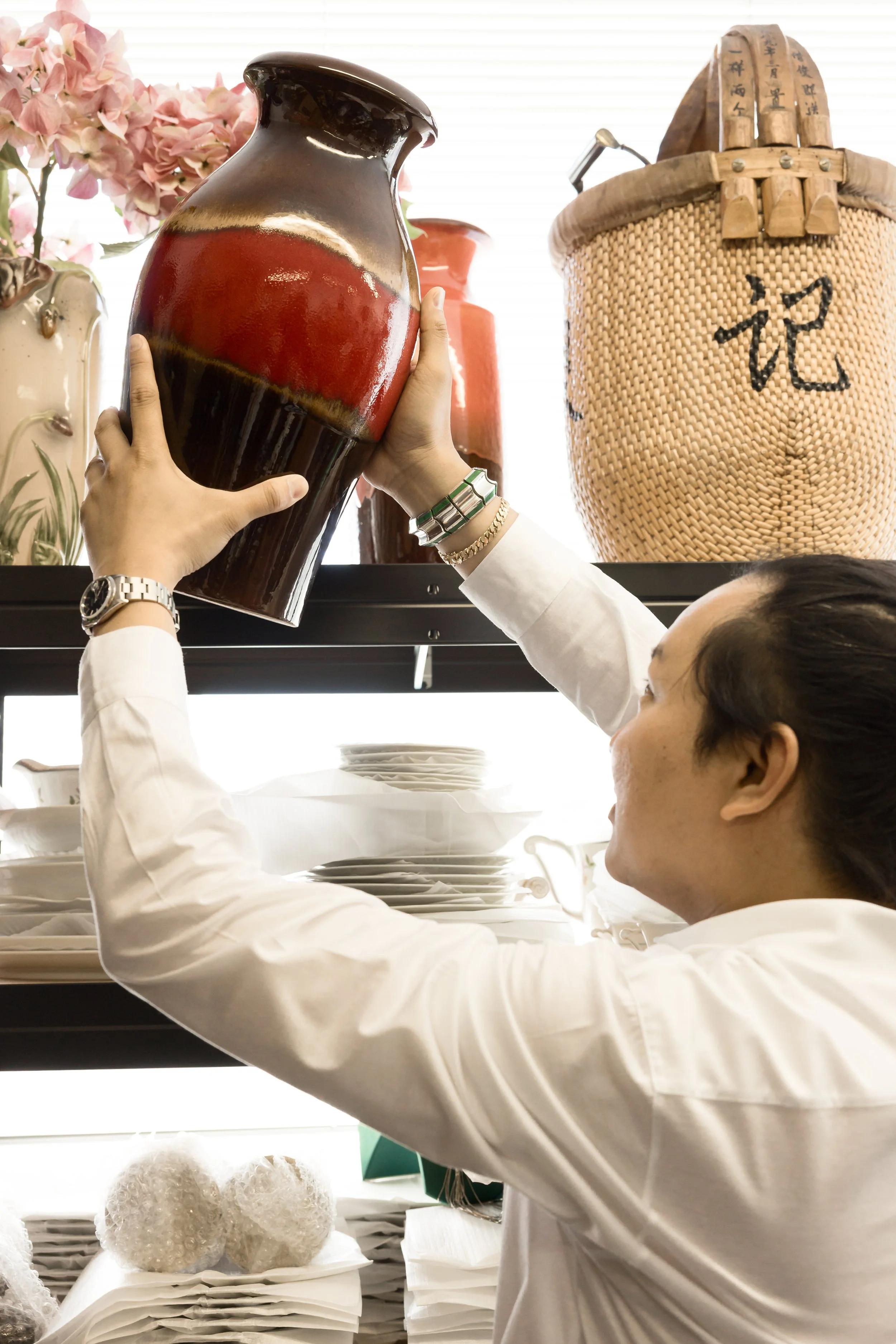 Antiques shop owner reaches for a mid century red vase - marketing photography by Sian T Photography, Esher Surrey