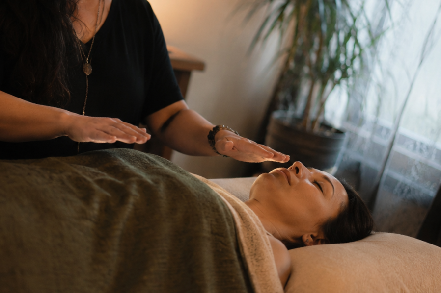 A woman receiving a Reiki session at a wellness center, lying on her back with eyes closed while a practitioner gently places hands above her. Reiki, two harbors Mn, massage and reiki, Traditional Usui Reiki, Reiki master practitioner.