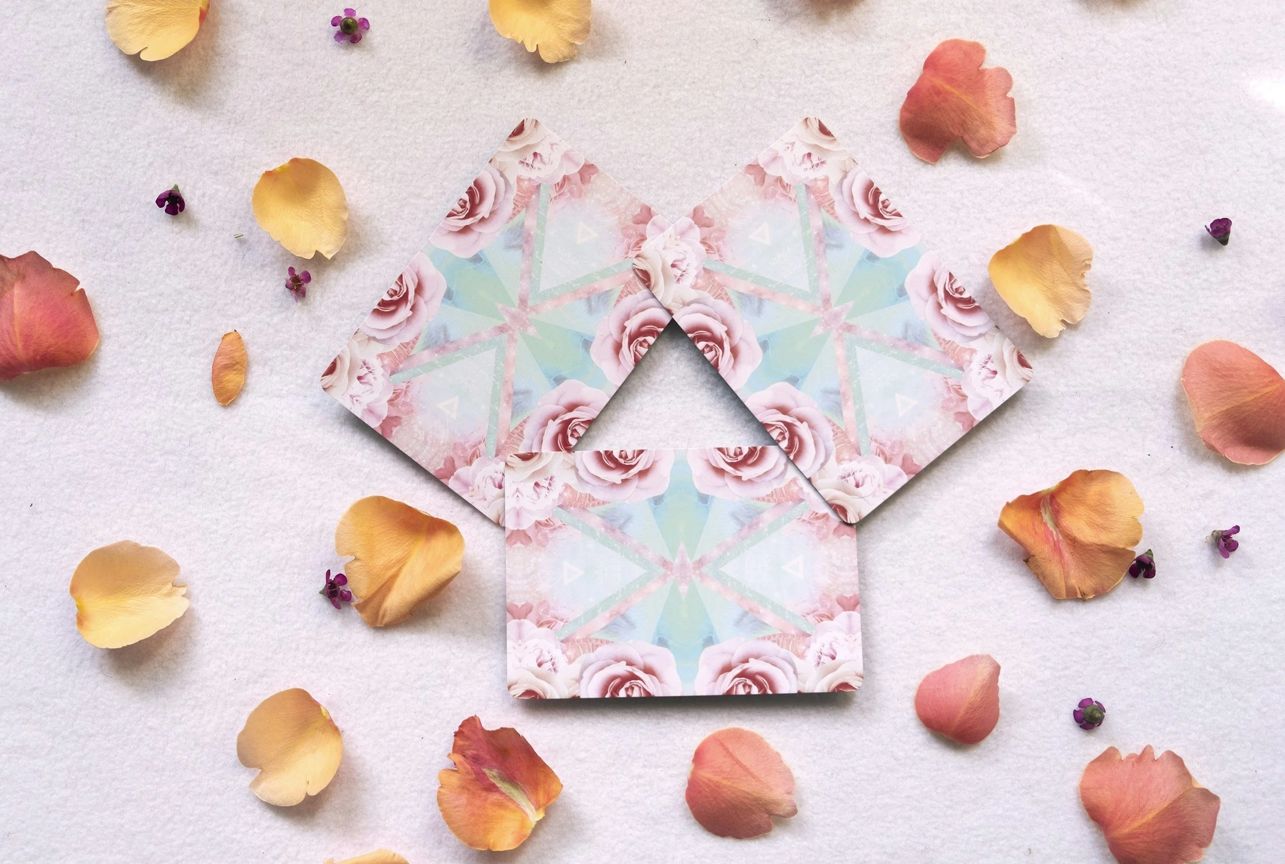 Pieces of paper with pink roses and geometric patterns surrounded by scattered orange and pink rose petals and small purple flowers on a white background. Tarot card reading, oracle card reading, Divination reading, card deck, two harbors Mn