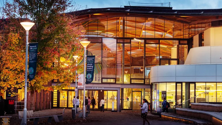 The front elevation of The Forum building at Exeter Universityen table in a café, laughing and working on laptops with drinks. A handwritten notebook and a brown leather notebook are on the table.