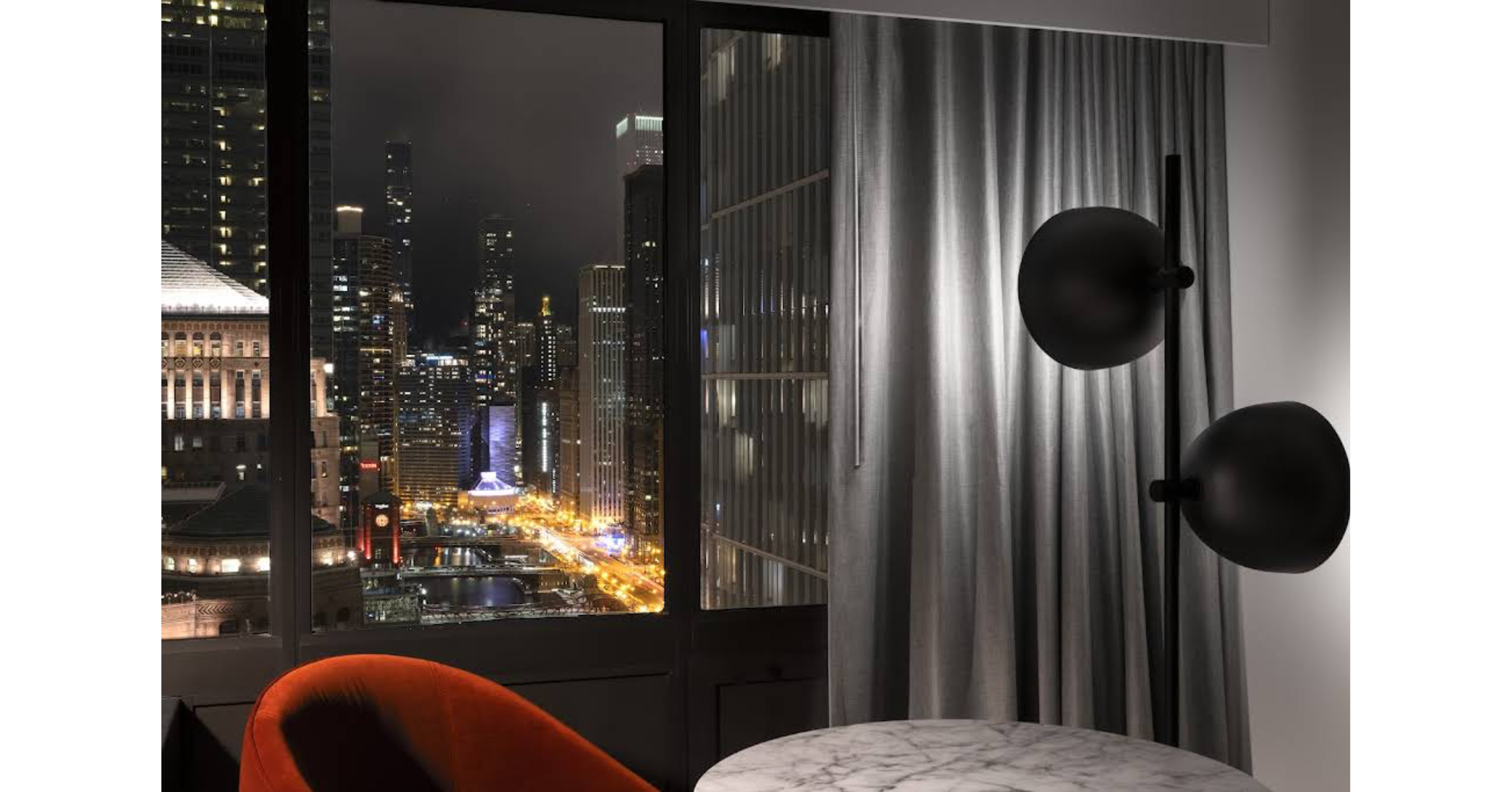 Photo looking out the window of a hotel room at the Chicago River lit up at night
