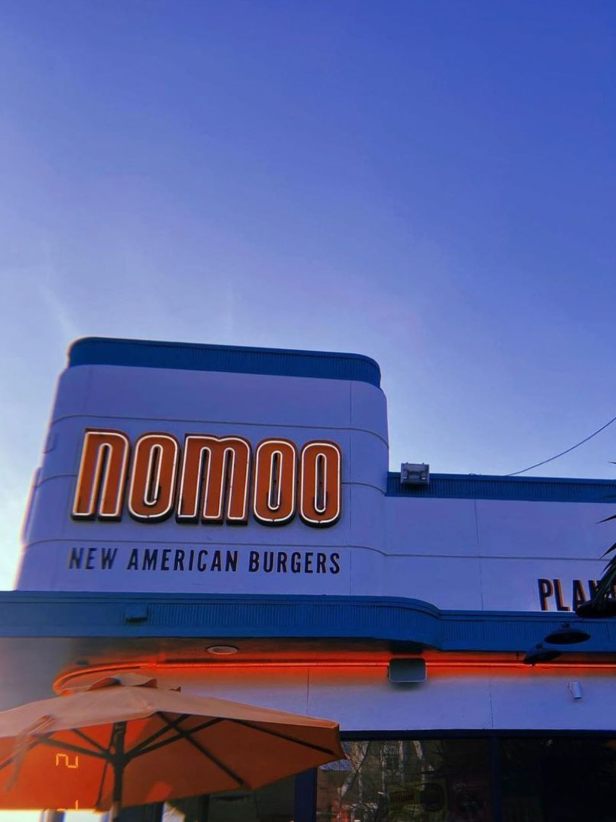 Sign for Nomoo, a burger restaurant, with the tagline 'New American Burgers' and an umbrella visible in the foreground.