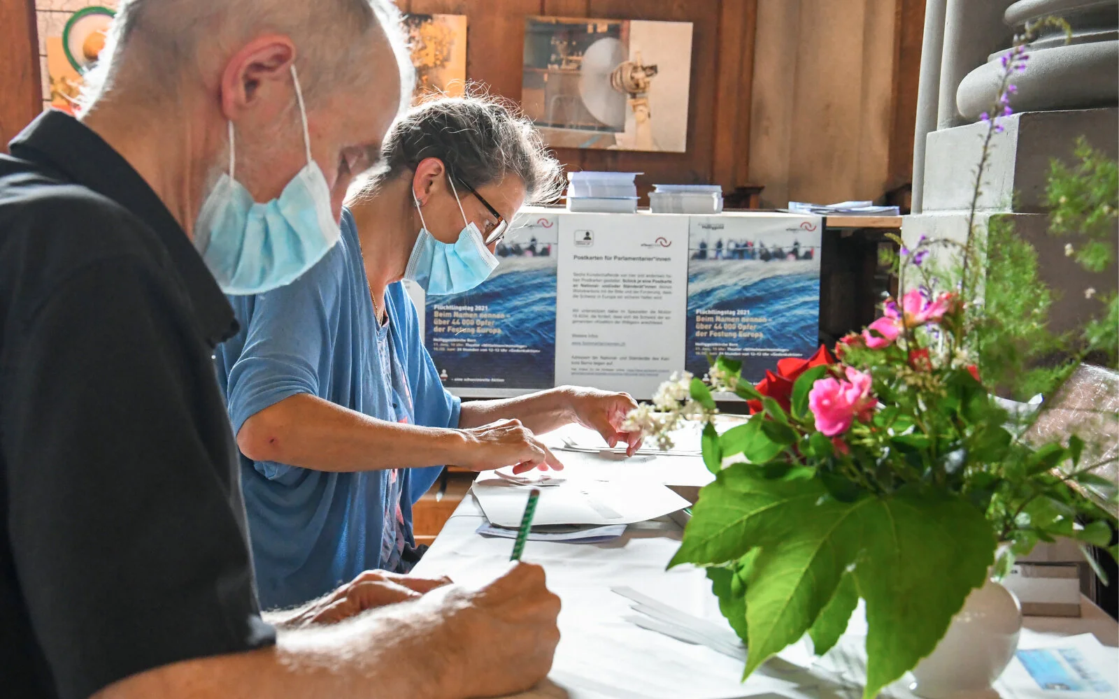 Zwei Personen sitzen konzentriert nebeneinander an einem Tisch in der Heiliggeistkirche übertragen handschriftlich die Einträge der «List of Deaths» auf Stoffstreifen
