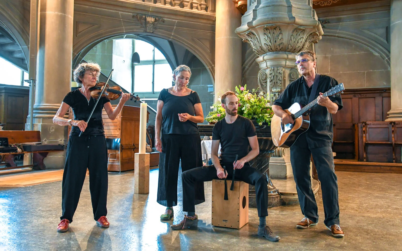 Vier Mitglieder der Band Schlamassel spielen ein Stück: Gesang, Violine, Perkussion und Gitarre, alle sind in schwarz gekleidet