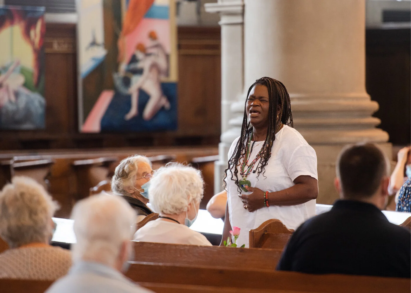 Eine Frau steht singend im Gang der Heiliggeistkirche zwischen den Bankreihen, wo Menschen sitzen und ihrem Gesang zuhören.