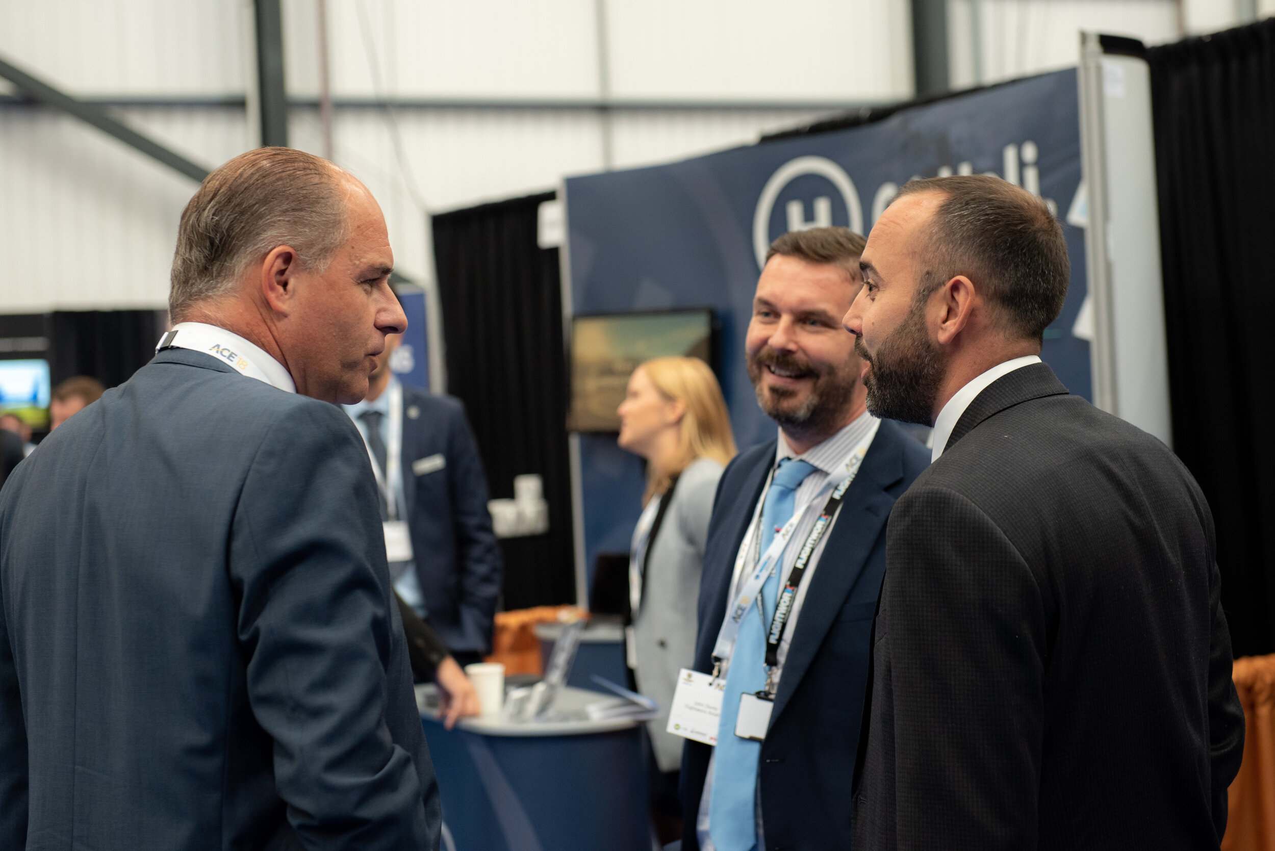 Group of business professionals interacting at a trade show or convention with a booth in the background.