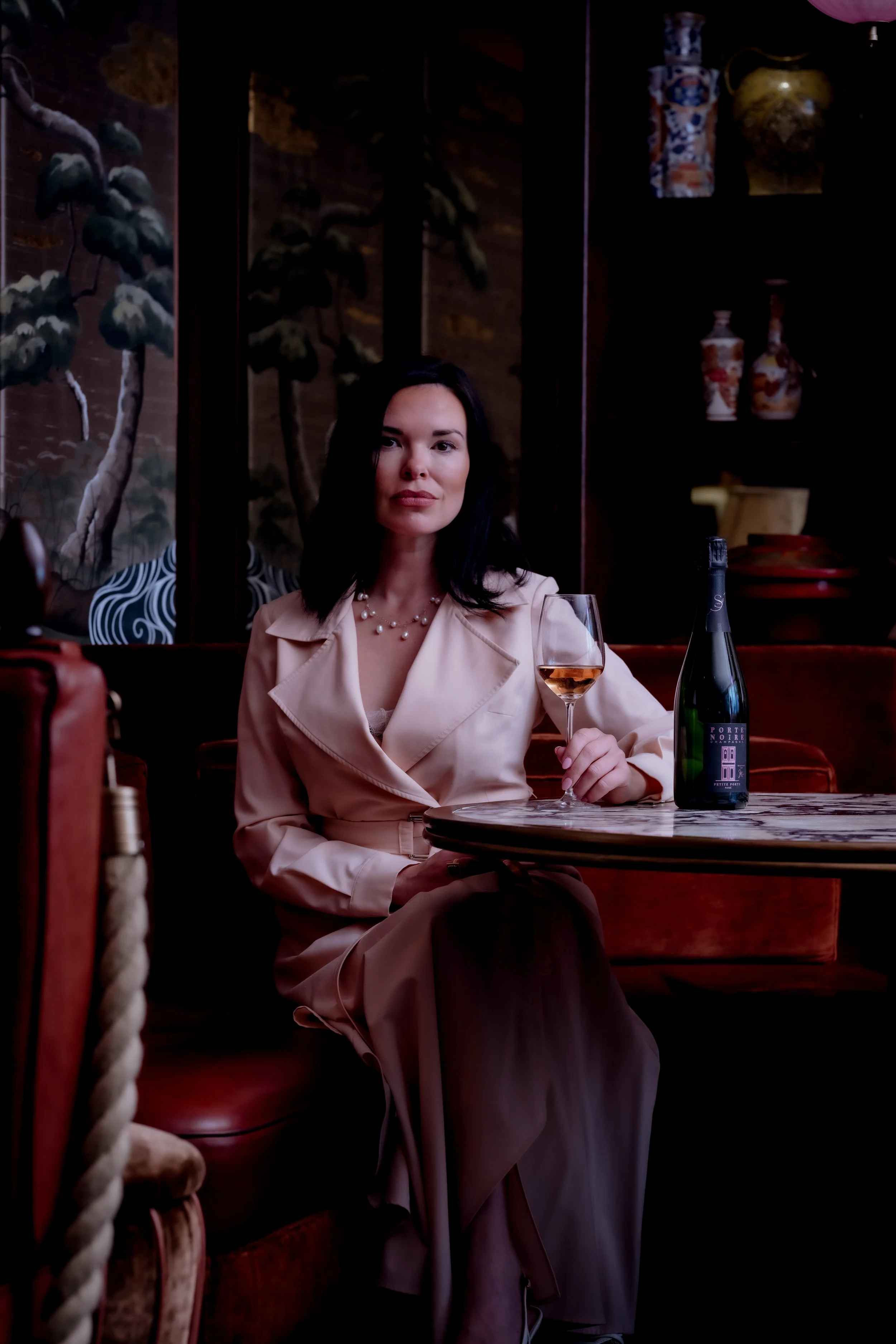 Libby Brodie, in sitting at a marble table with a bottle of rose champagne, wearing a sophisticated outfit with an air of authority on all things wine