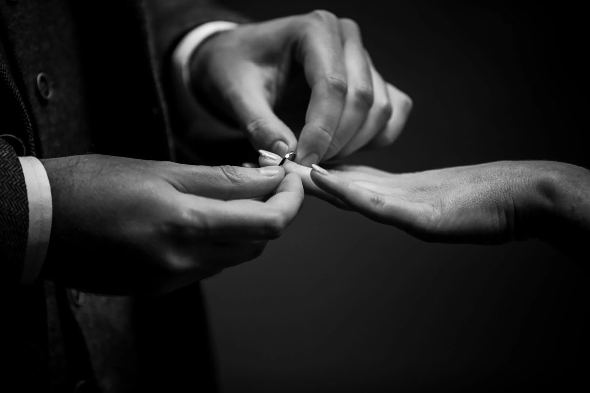 Close-up of a person placing a ring on another person's finger during a wedding ceremony.
