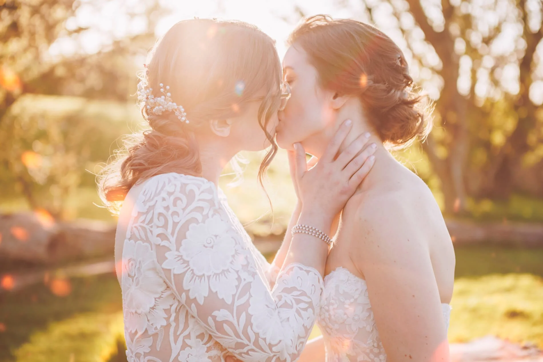Two women sharing a kiss outdoors during sunset, both in wedding dresses. Newton Hall wedding photographer. Low Newton by the Sea