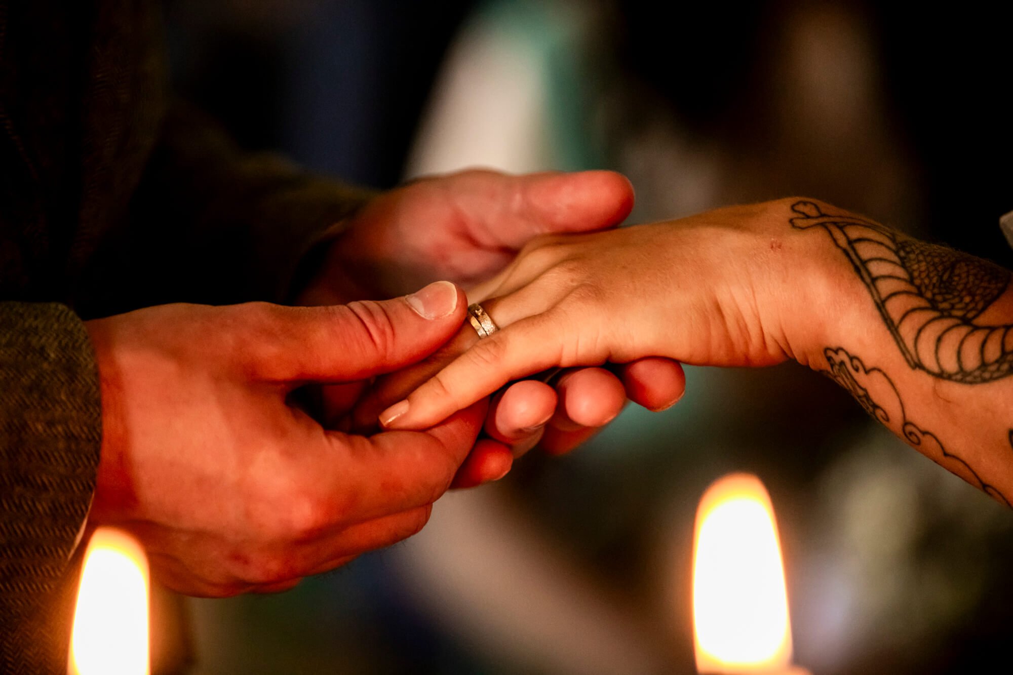 Two hands, one with a tattoo, hold each other during a candlelit ceremony. One hand wears a wedding ring. Newcastle Castle wedding photography