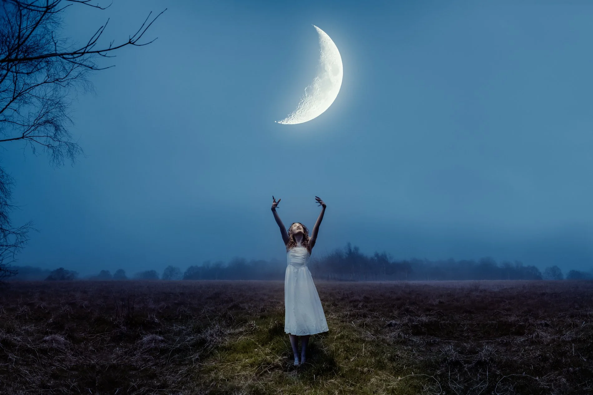 A woman in a white dress standing on a dirt path in an open field, reaching up towards the sky where a crescent moon is visible with a star nearby, under a clear blue night sky.