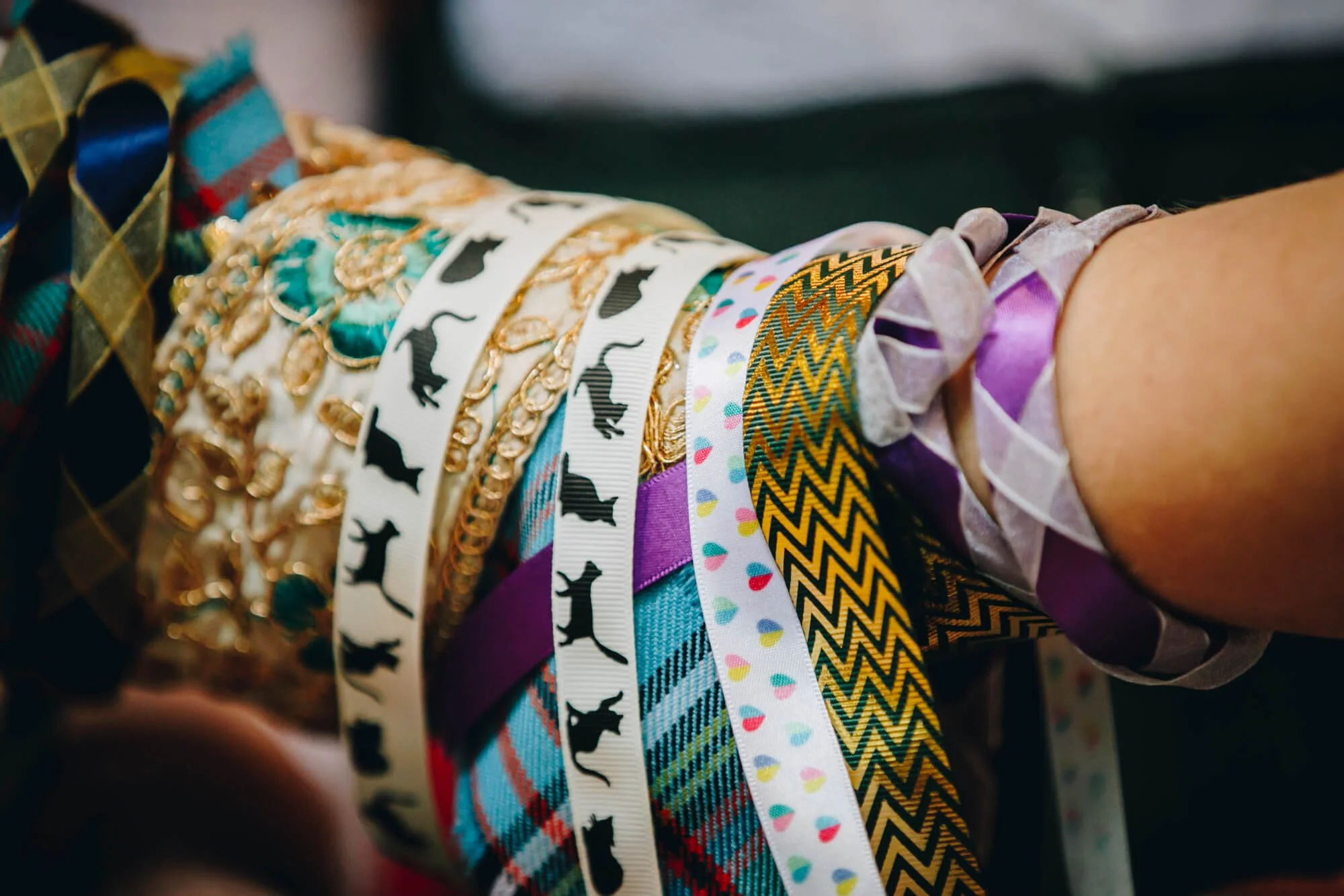 A collection of colourful ribbons draped over two people's arms in a handfasting ceremony, featuring various patterns including cats, diamonds, polka dots, plaid, and chevron.