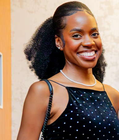Smiling woman with curly hair wearing a black sequined dress and pearl necklace