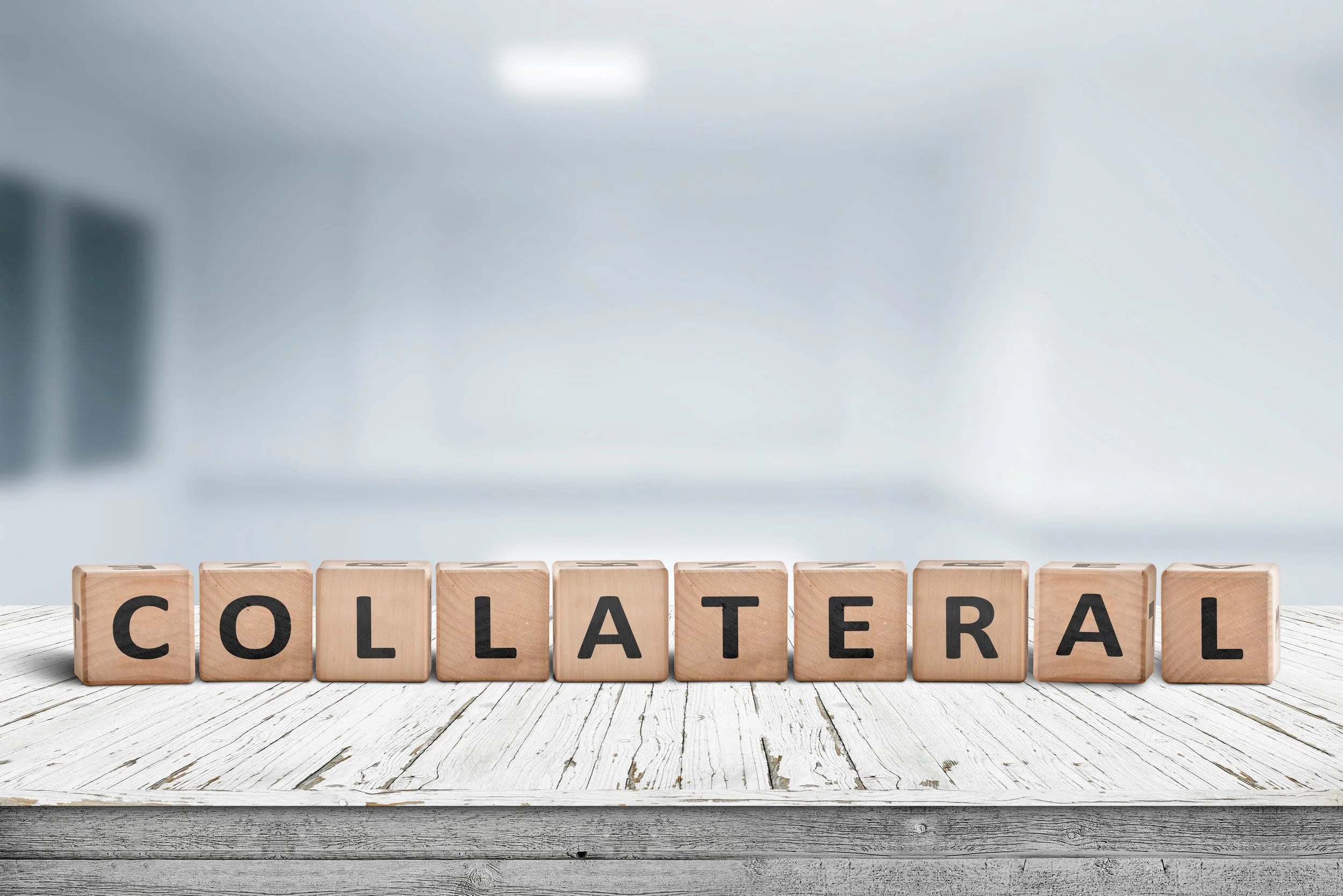 Wooden blocks spelling "COLLATERAL" on a white wooden table.