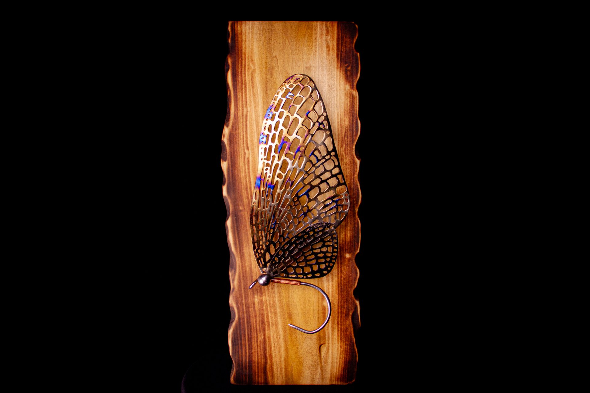 A mayfly with intricate cutout details, mounted on a wooden plaque. A luxury handcrafted metal sculpture designed for discerning art collectors. 