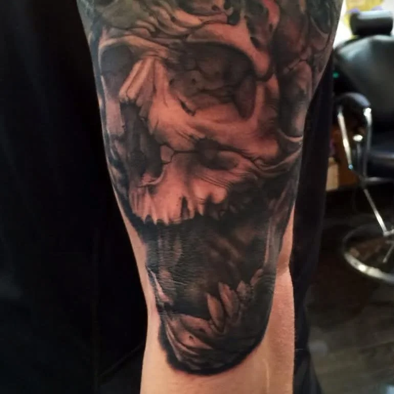 Close-up of a tattoo on a person's arm, depicting a realistic, detailed face of a roaring tiger or lion with its mouth open, showing sharp teeth.