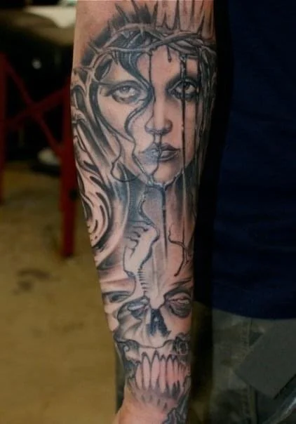 Tattoo of a woman's face with long hair, a skull, and a snake on an arm.