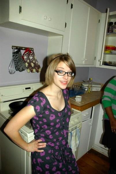  Pictured: Phoebe in 2009, a university hipster. She stands in a kitchen wearing a navy dress with purple leopard print, thick rimmed glasses, and a thin headband. Photo credit:  Nadine Maher  