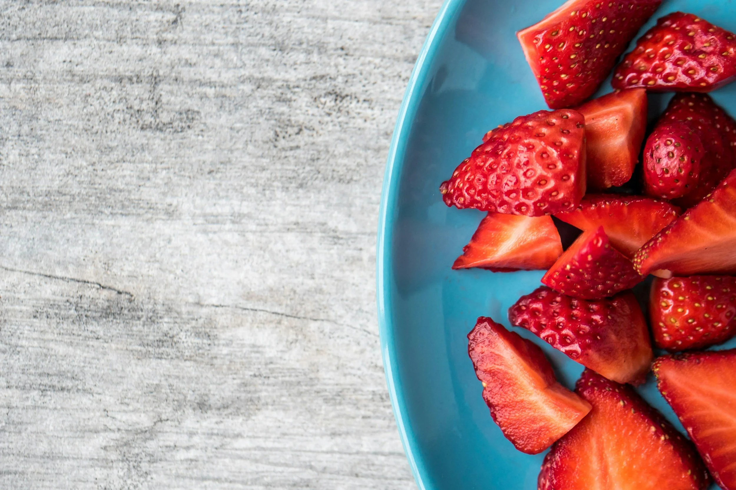 Sliced strawberries in a blue bowl on a wooden surface.