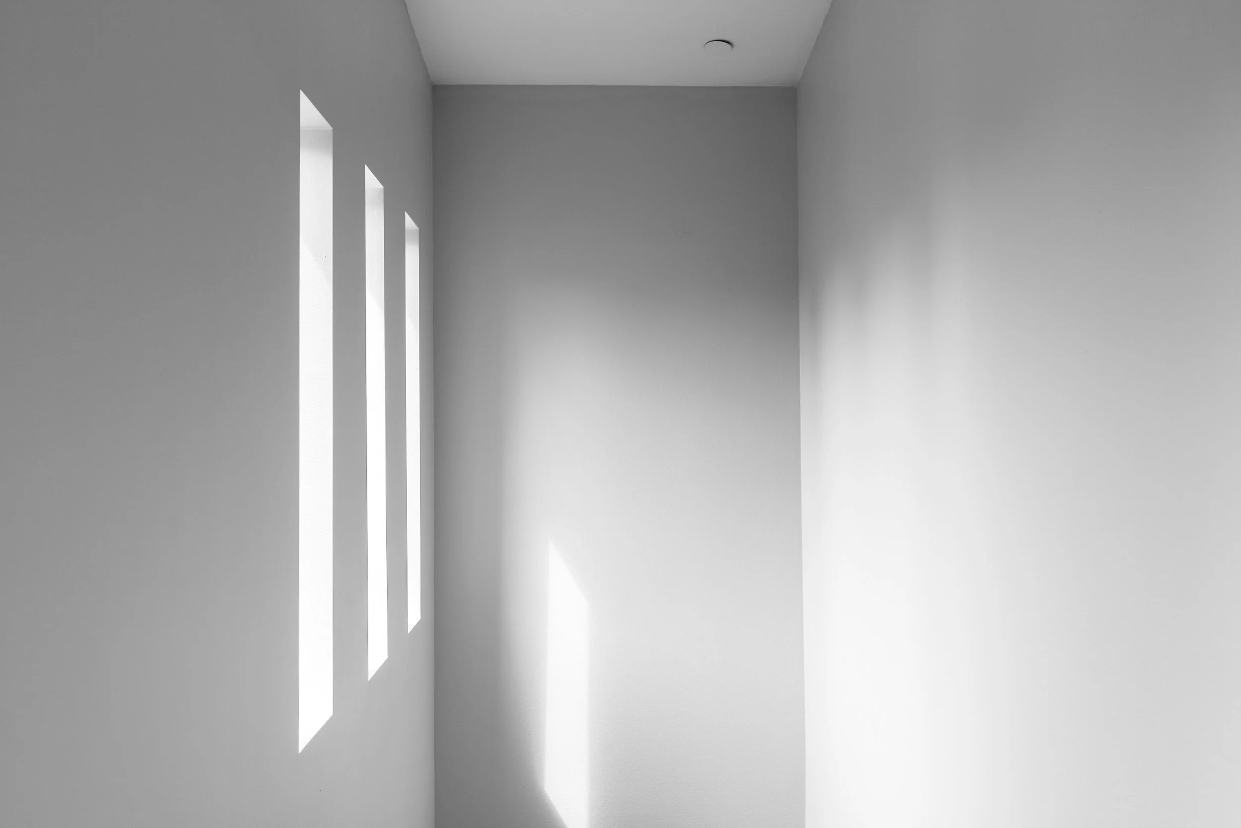 Natural light entering a quiet minimalist room, creating vertical shadows on the wall