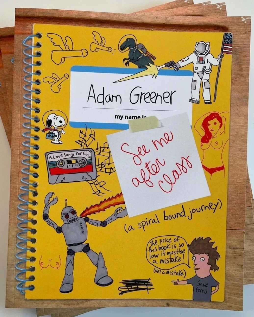 Yellow spiral-bound notebook cover decorated with doodles of a robot, astronaut, dinosaur, music cassette, Snoopy with a backpack, a nude woman outline, a woman with a speech bubble, and a small girl. The central white label reads 'Adam Greener my name is' and a sticky note with red handwriting says 'See me after class.' The text at the bottom says '(a spiral bound journey)'.