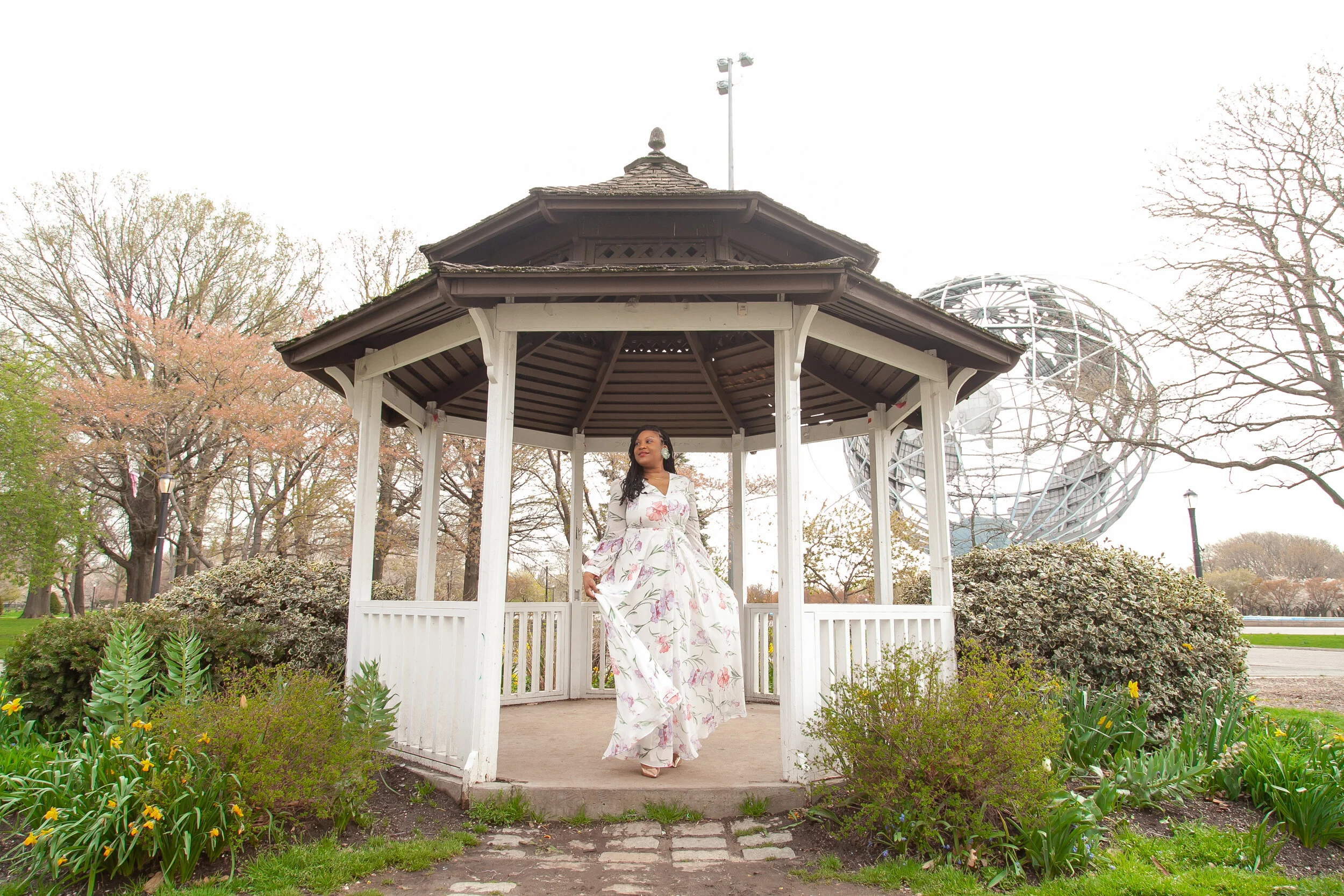 woman in floral dress standing in gazebo surrounded by flowers and shrubs