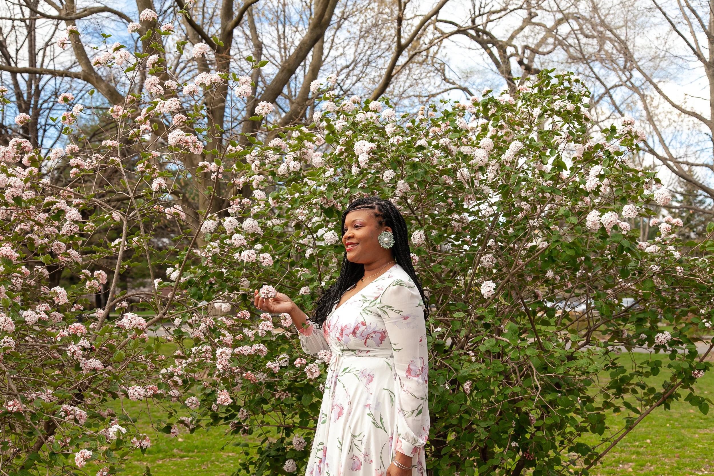 woman in floral dress touching cherry blossom tree