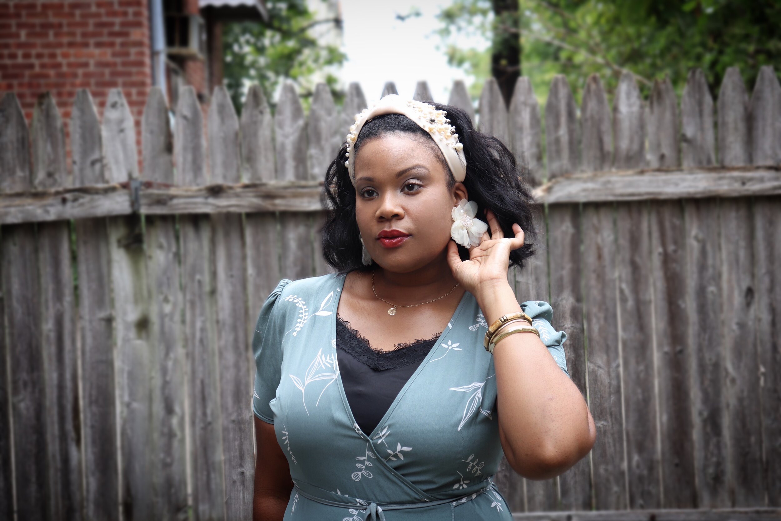 woman poses in green floral dress gently touching her off white tulle pearl stud earring