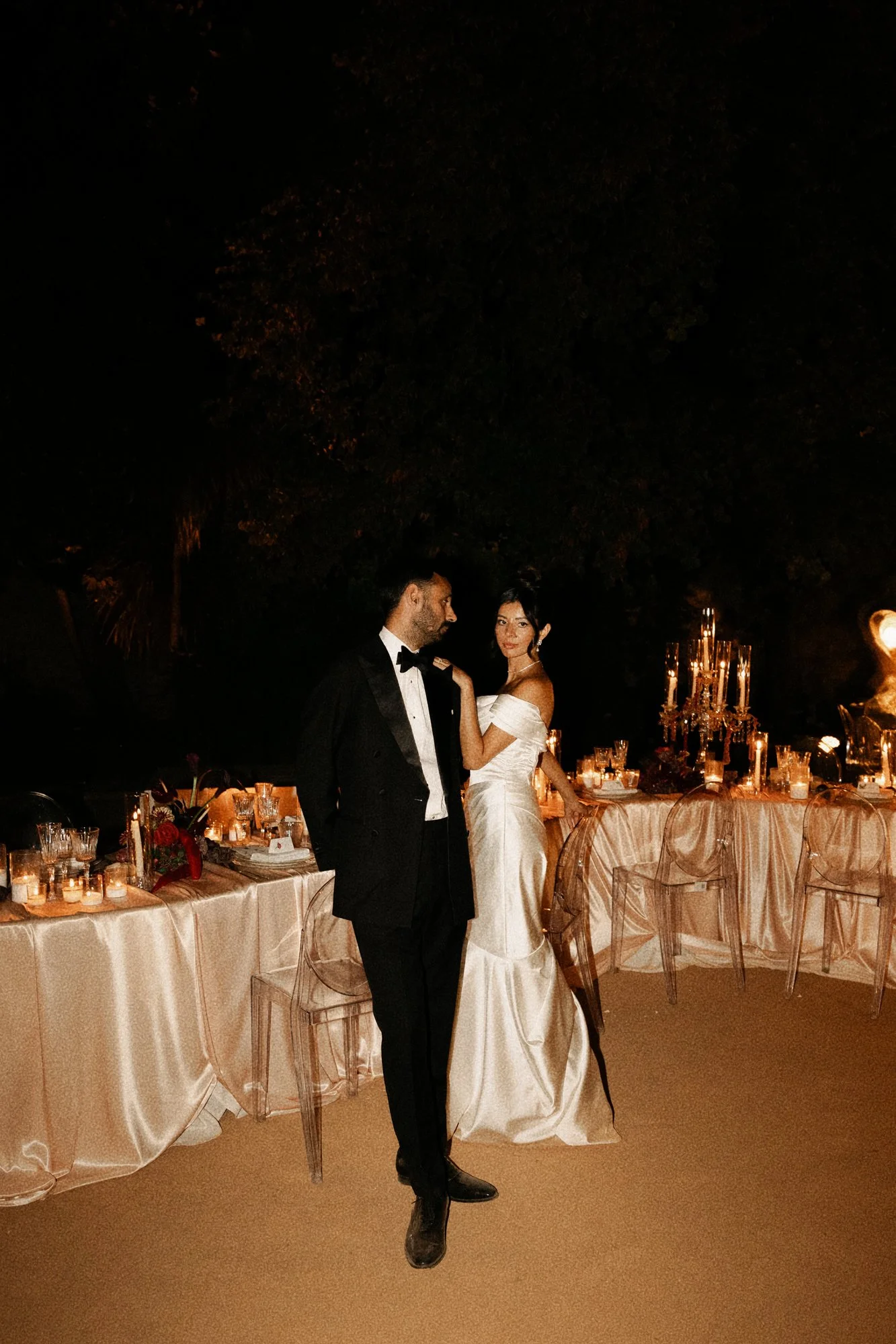 A newlywed couple, a man in a tuxedo and a woman in a white wedding dress, dancing at a wedding reception at night with decorated tables and candle lighting photographer by editorial Spain wedding photographer