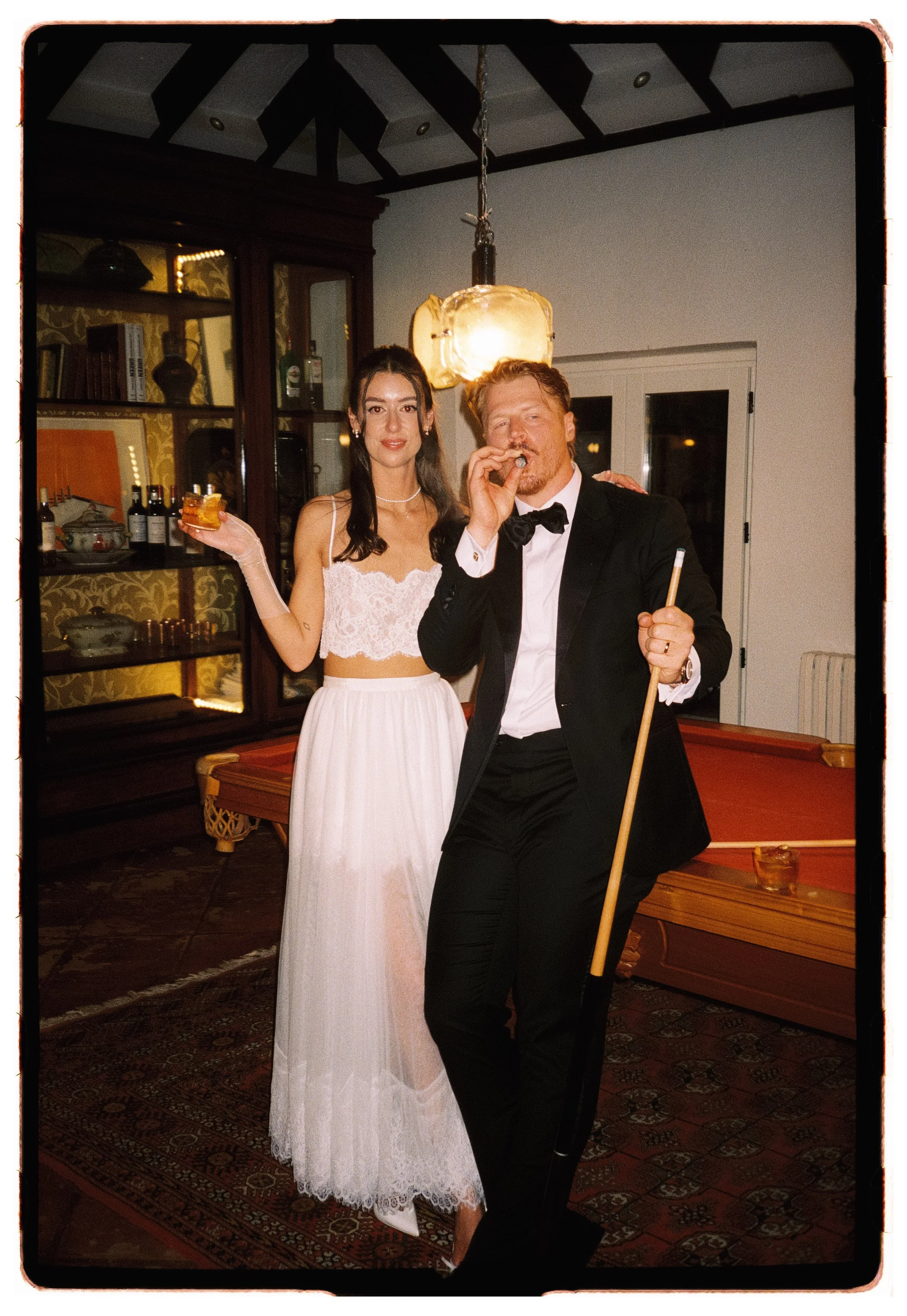 Late night pool game, couple holding cocktails and smoking cigars captured by Spain wedding film photographer