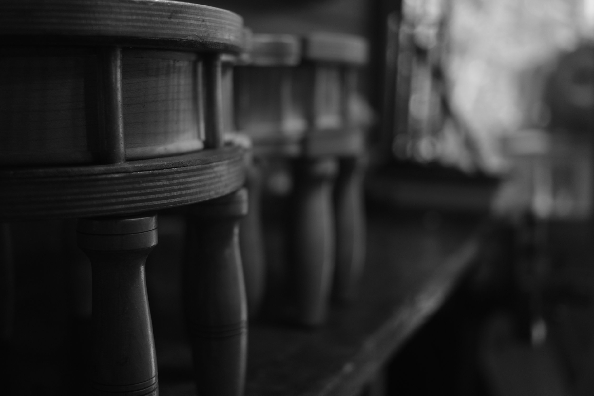 Black and white close-up of a row of wooden stools with turned legs, lined up on a wooden surface.