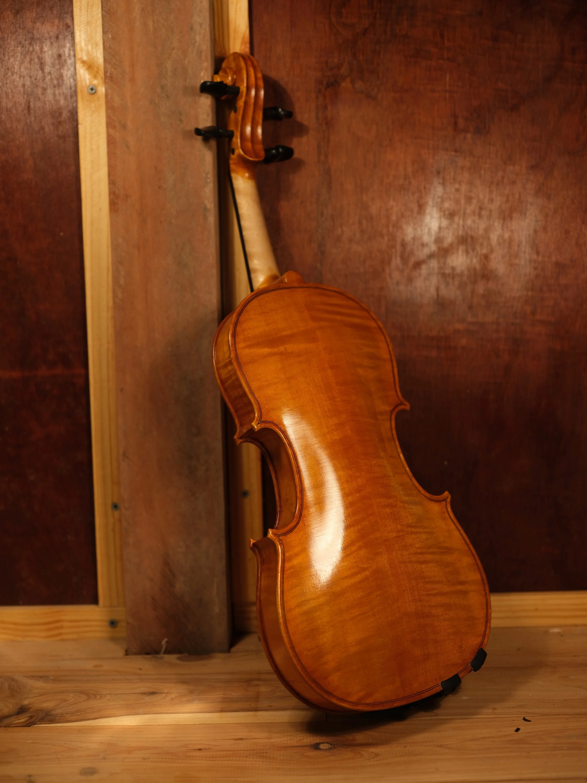 A wooden violin resting on a wooden surface with a wood-paneled background.
