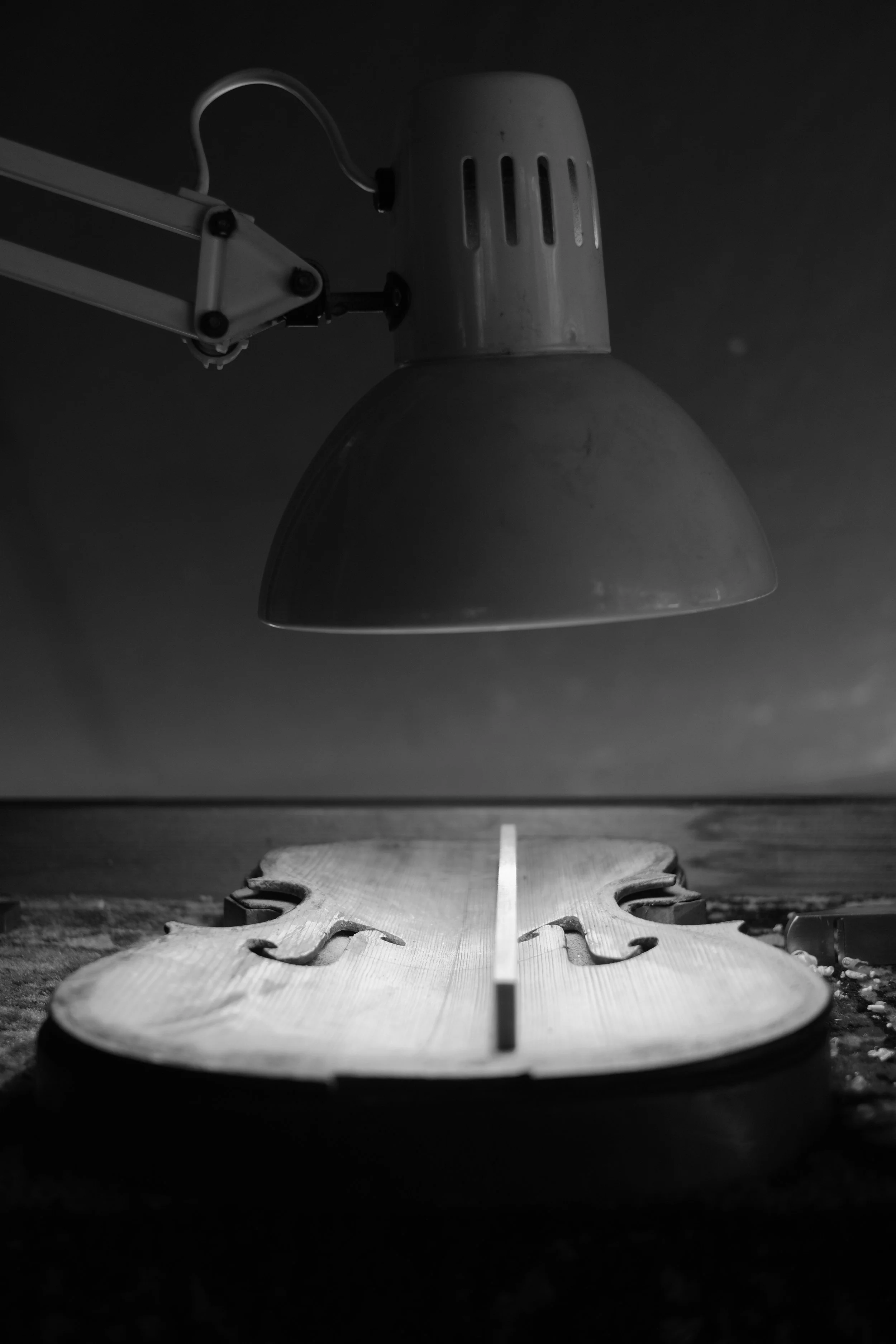 Black and white photo of a wooden violin body and a lamp above it, illuminating it.