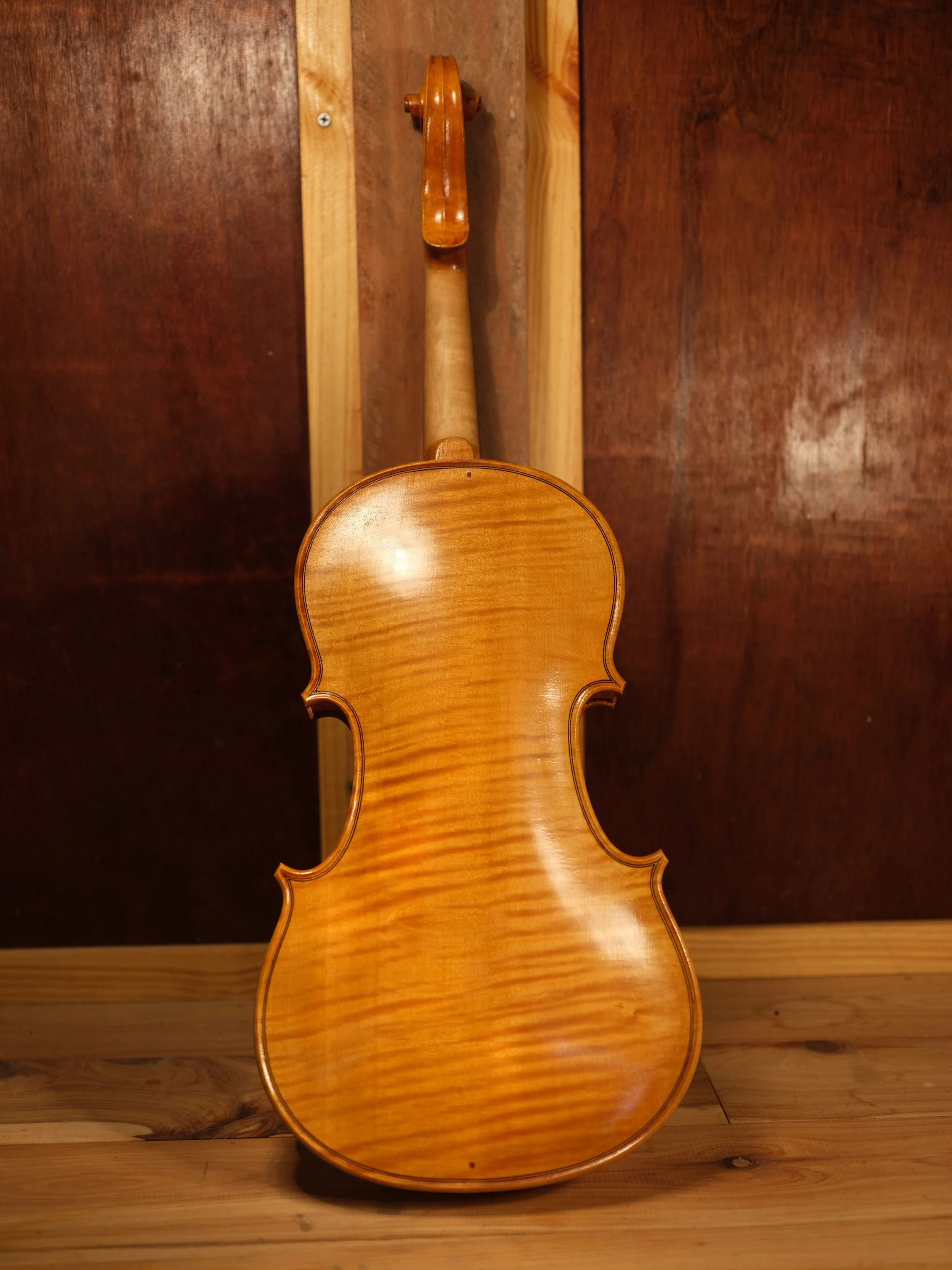 Back of a wooden violin leaning against a wooden wall.